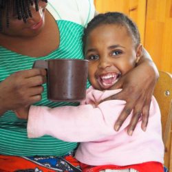 Young girl hugging her caregiver and smiling while her caregiver holds a mug