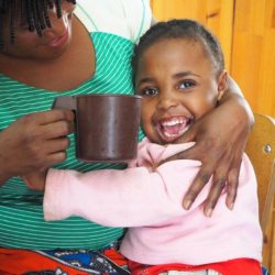 SPOON Foundation Young girl hugging her caregiver and smiling while her caregiver holds a mug