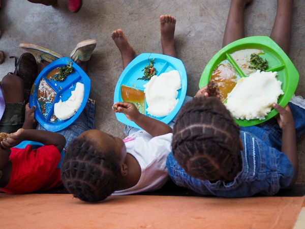 Children in Zambia sitting on the floor and eating from plates with well-rounded meals