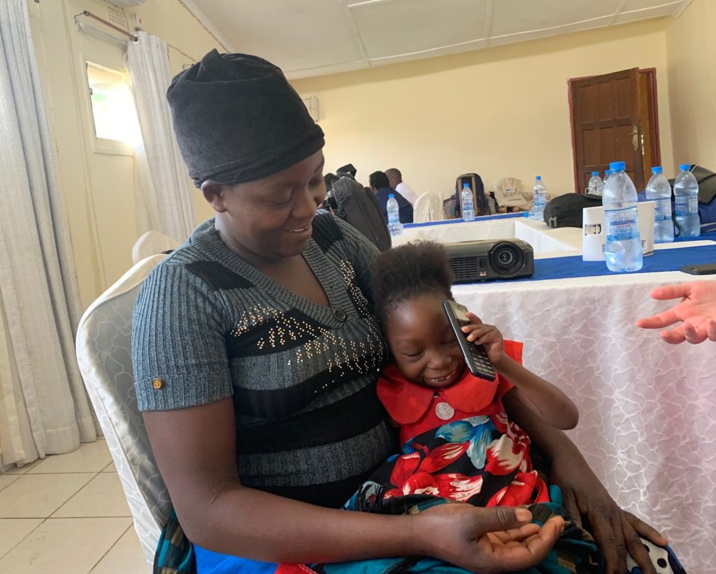 A mother and child with disabilities in Zambia. The child is sitting on the mother's lap and is holding the mother's cell phone, both are smiling