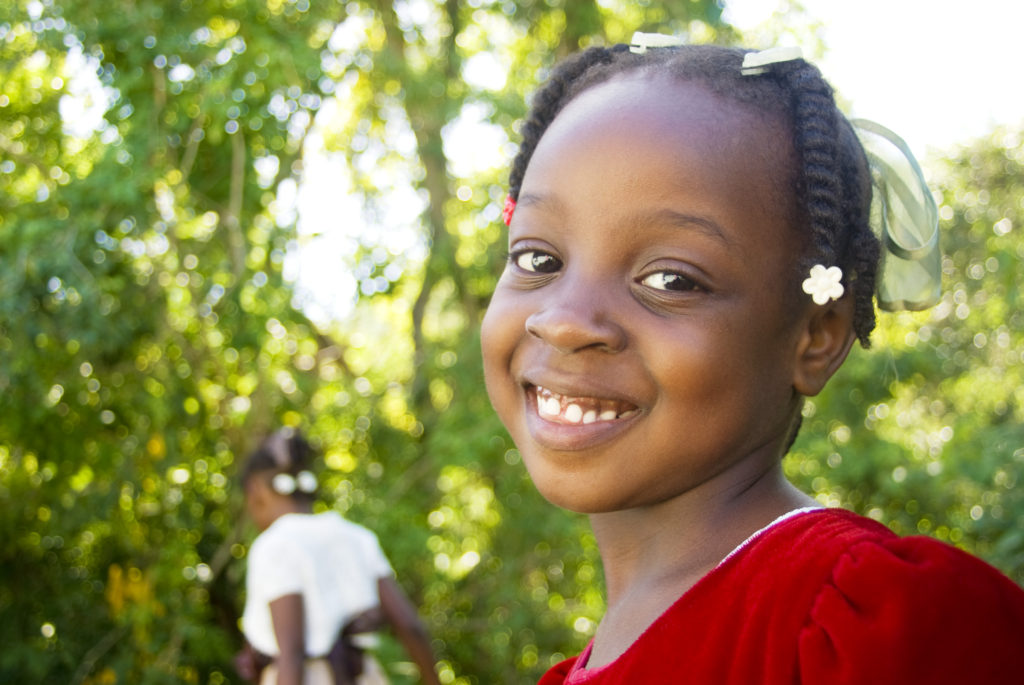 Young girl from Haiti smiling in a red shirt
