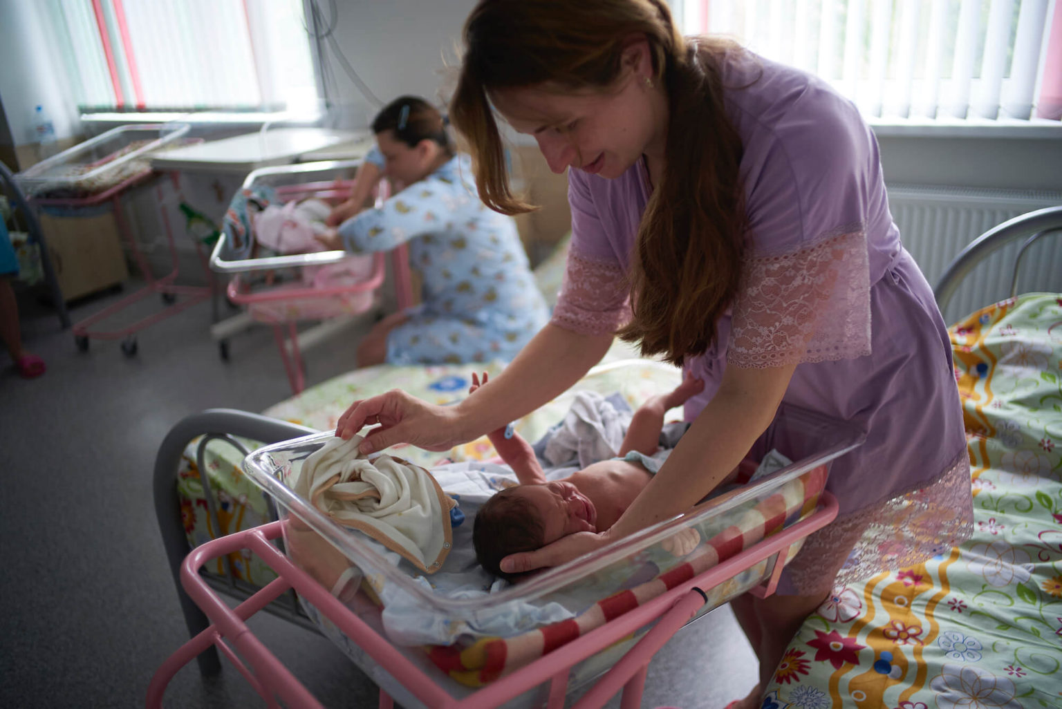 A caregiver in Belarus smiling and reaching to hold a small baby in a bed