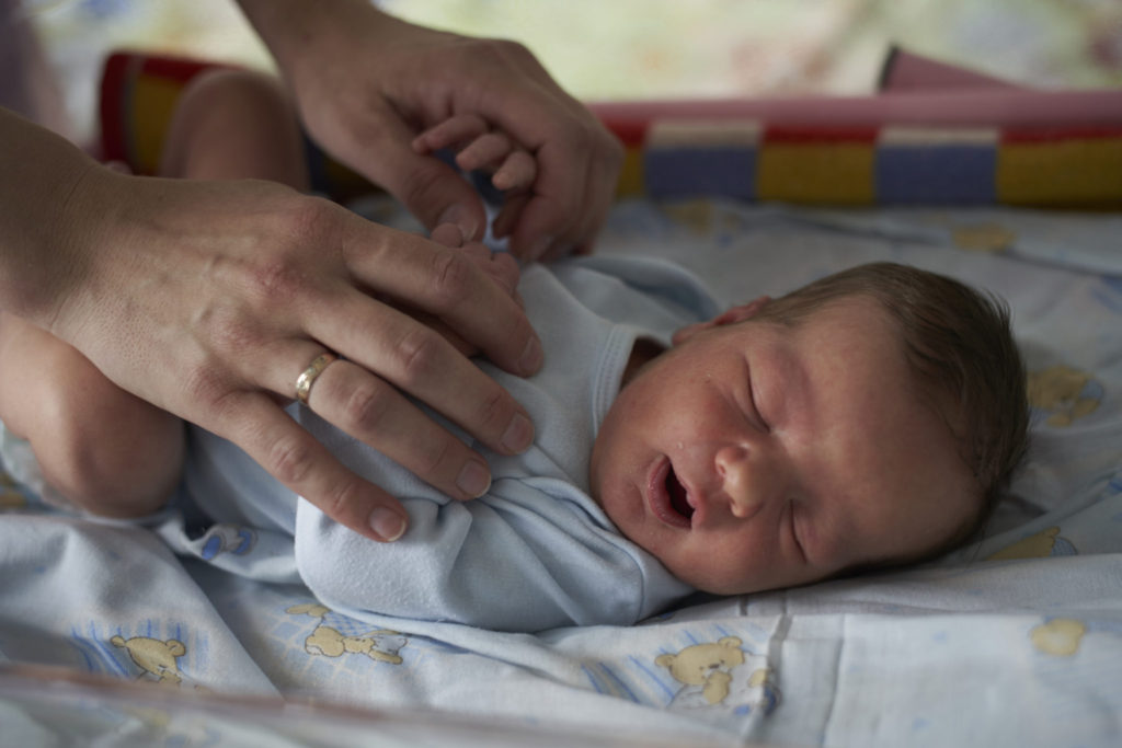 A caregiver holding hands with a newborn baby in Belarus