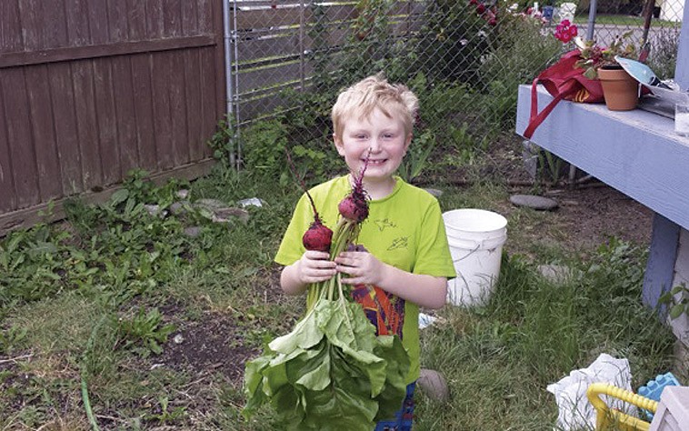 Young boy in Oregon standing in a backyard and holding two radishes
