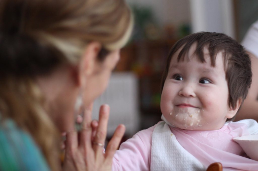 Young child with food on their mouth smiling and holding hands with an adult