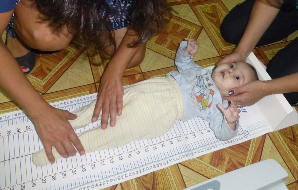 An infant child being measured for length on the floor with her head supported