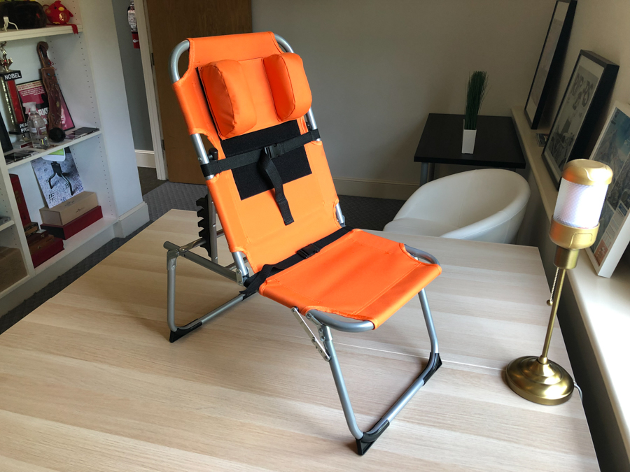 Prototype of the SPOON chair from the front: an orange, aluminum folding chair with padding on the sides and belts