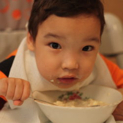 Young child eating out of a bowl with a spoon and wearing a bib