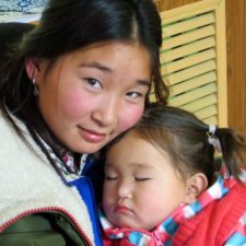 A smiling caregiver holding her young daughter, who is sleeping