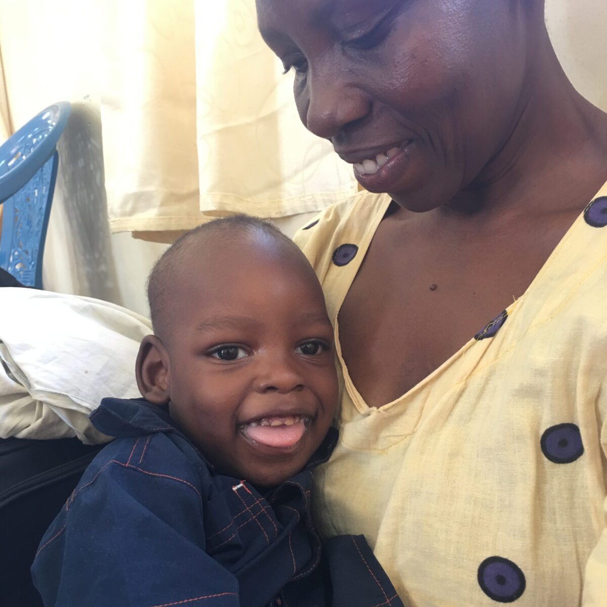 A young child with disabilities in Uganda sits on his mother's lap and both are smiling.